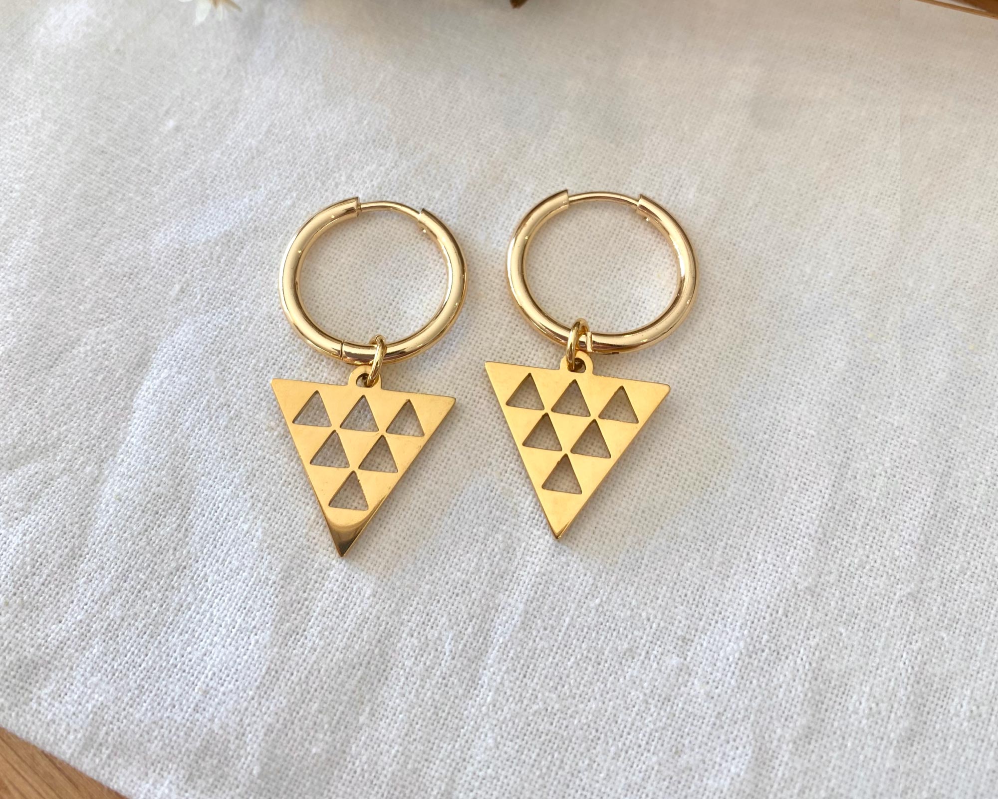 Gold hoop earrings with triangle charms on a light fabric background